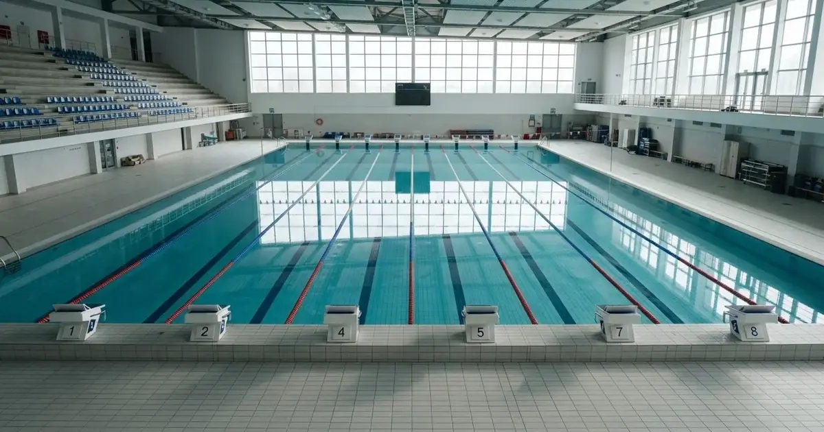 Pusty basen olimpijski z równymi torami i spokojną taflą wody, widok z trybun w jasnym świetle.